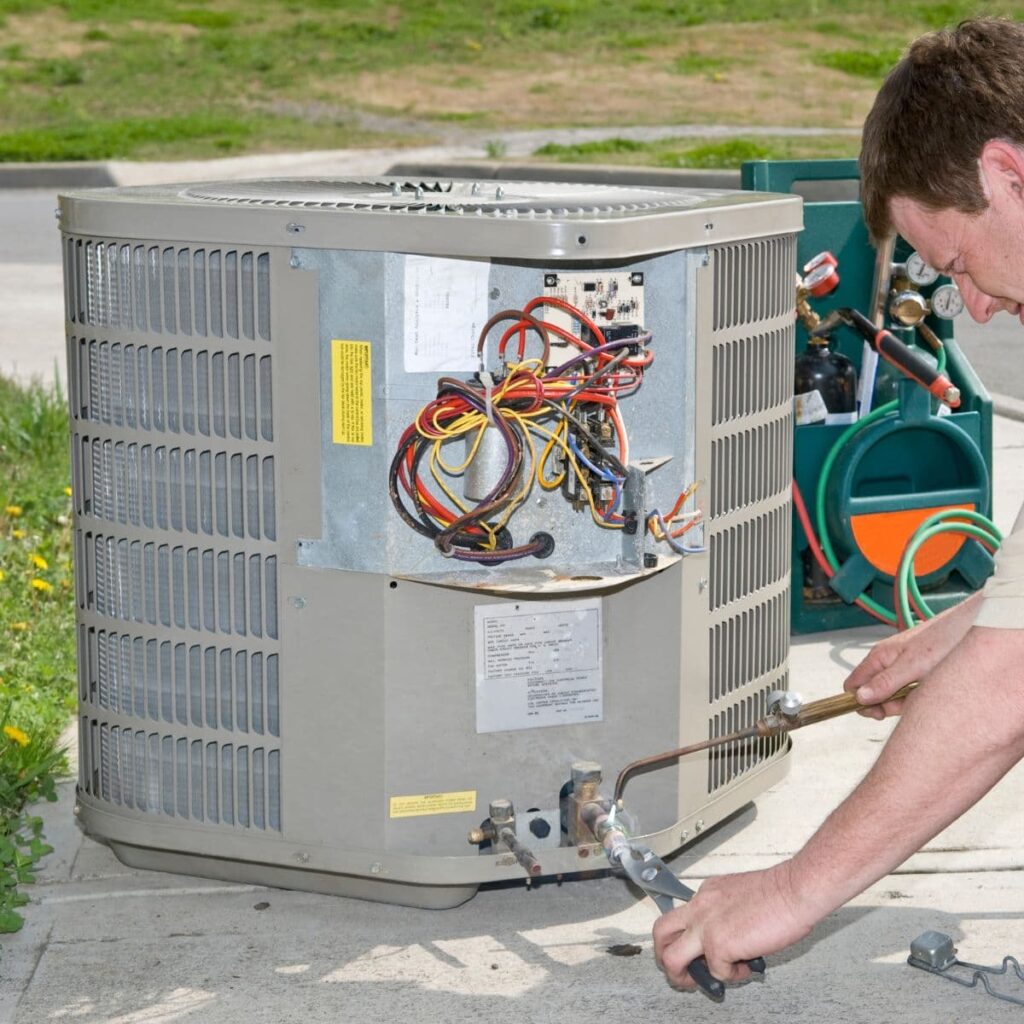 hvac technician holding two tools up against an outdoor hvac unit performing ac maintenance and repairs