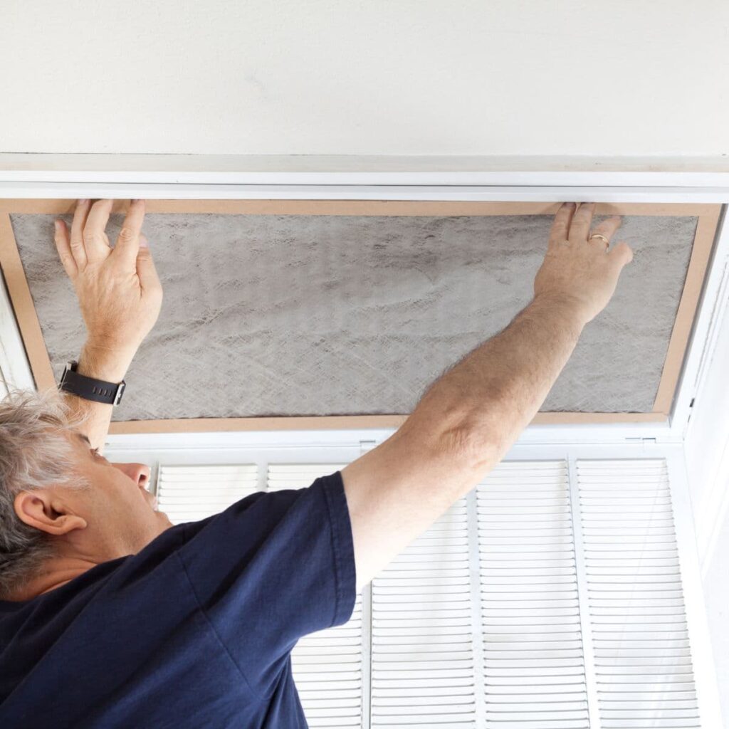 hvac technician reaching up to replace extremely dirty and full air filter