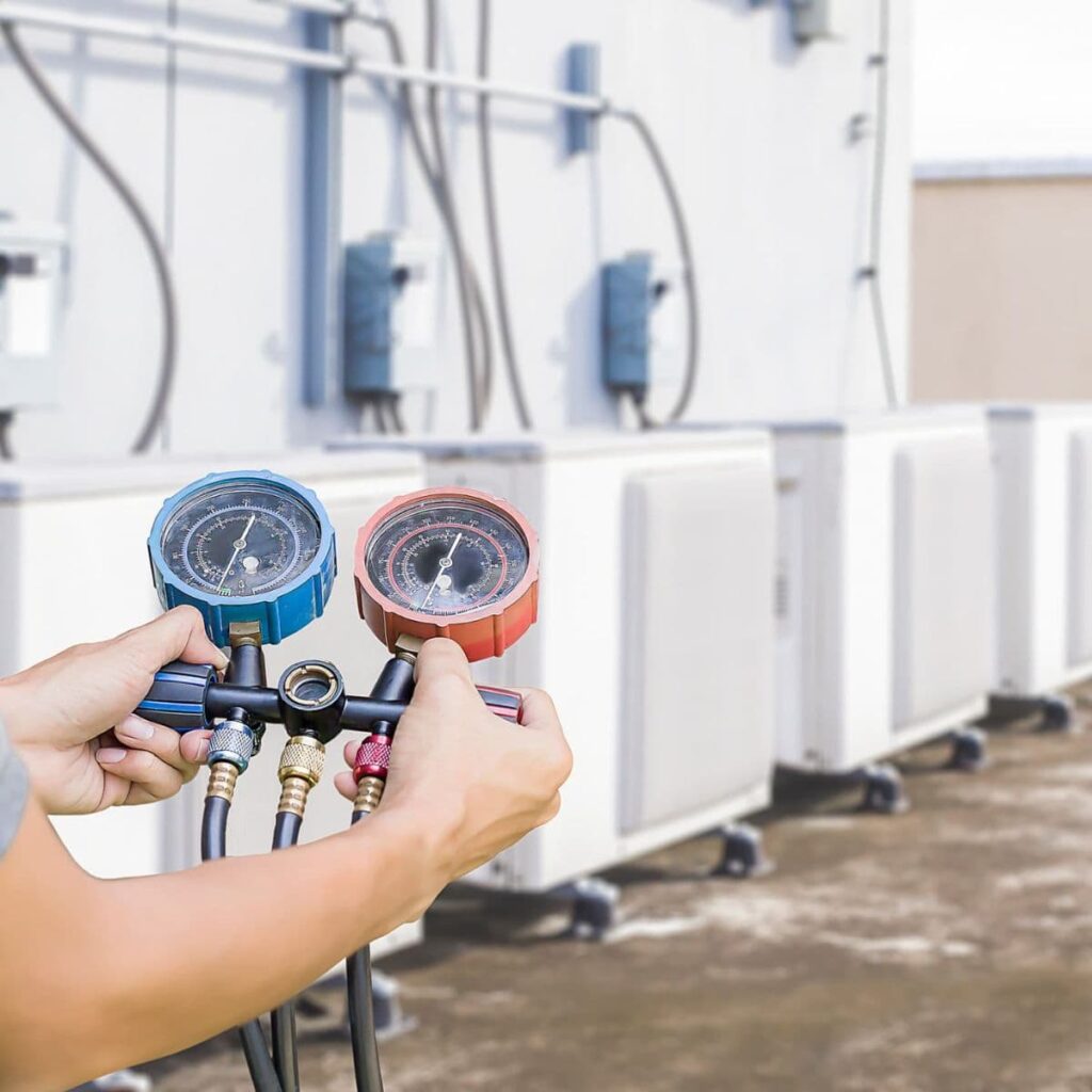 technician holding up a manifold pressure reader in front of a line of commercial units