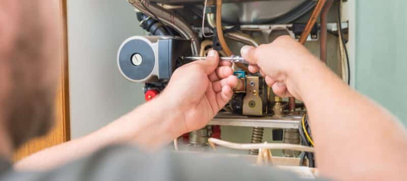 hvac technician using a tool to perform maintenance on an electrical furnace unit