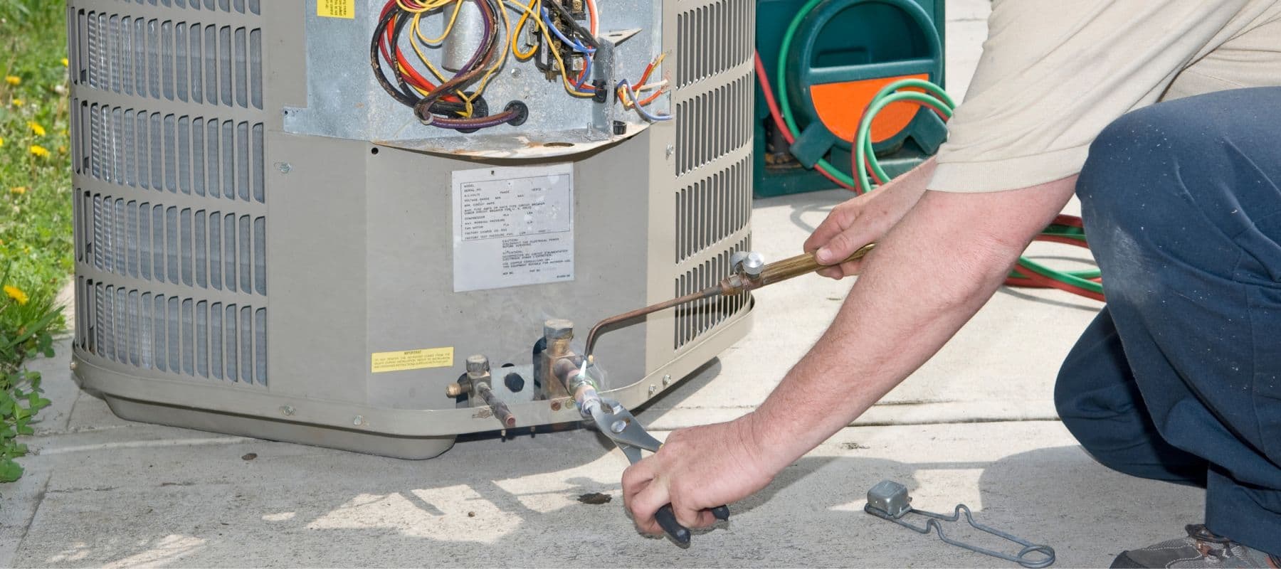 hvac technician holding two tools up against an outdoor hvac unit performing ac maintenance and repairs