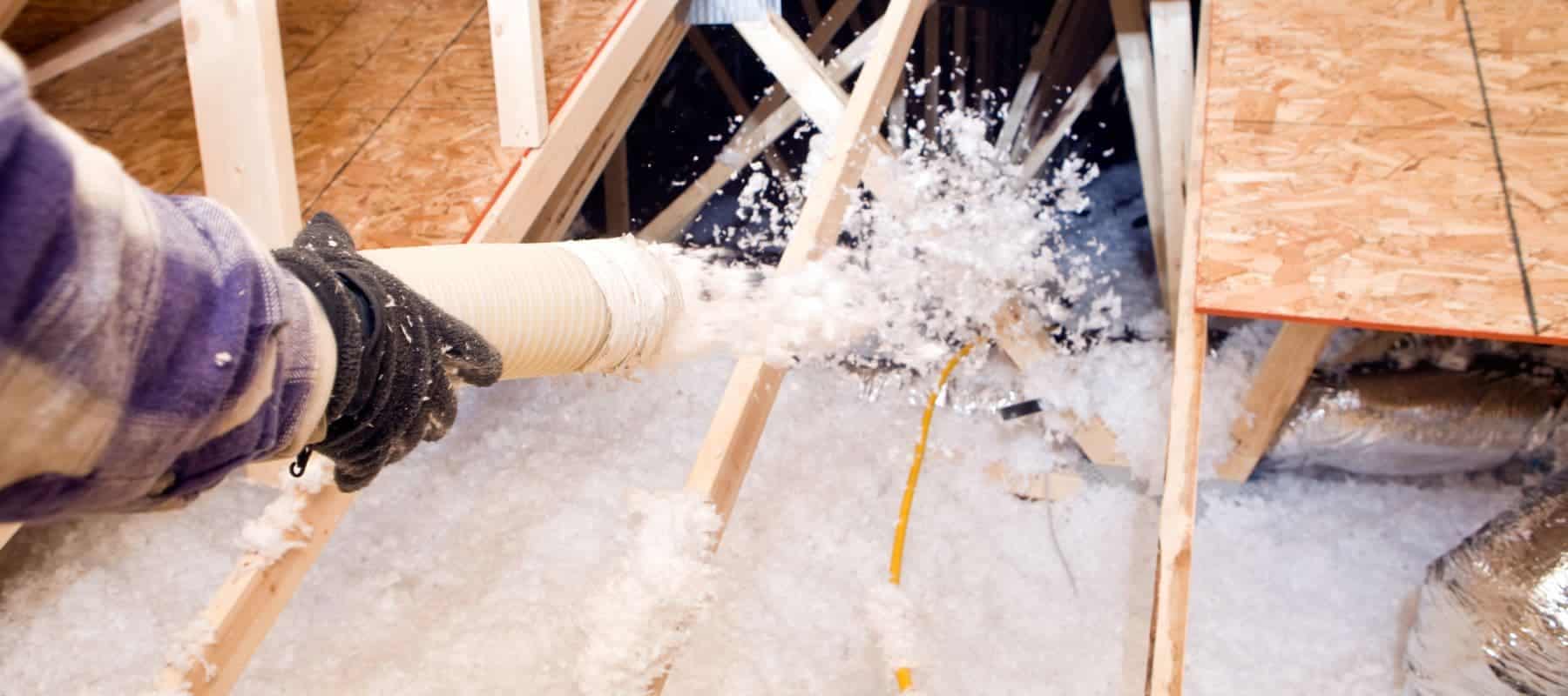 technician holding a large tube that has attic insulation blowing out of it as it's packing up the space