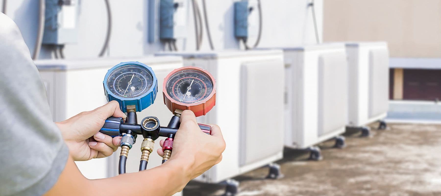 technician holding up a manifold pressure reader in front of a line of commercial units