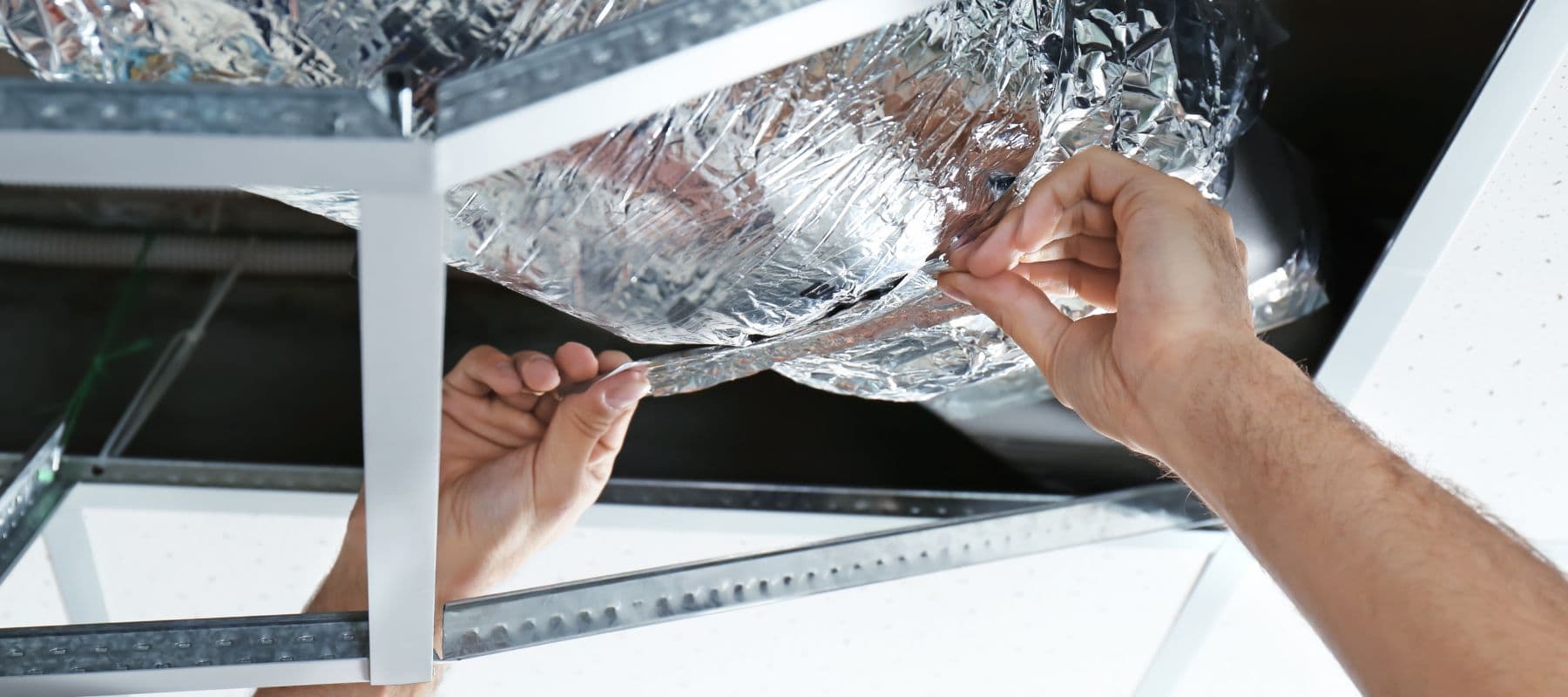 hands reaching up adding silver tape to air duct