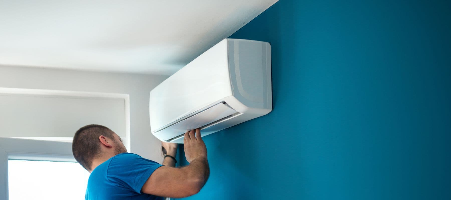 hvac technician looking thoroughly at a newly installed ductless ac unit that was installed on a blue wall
