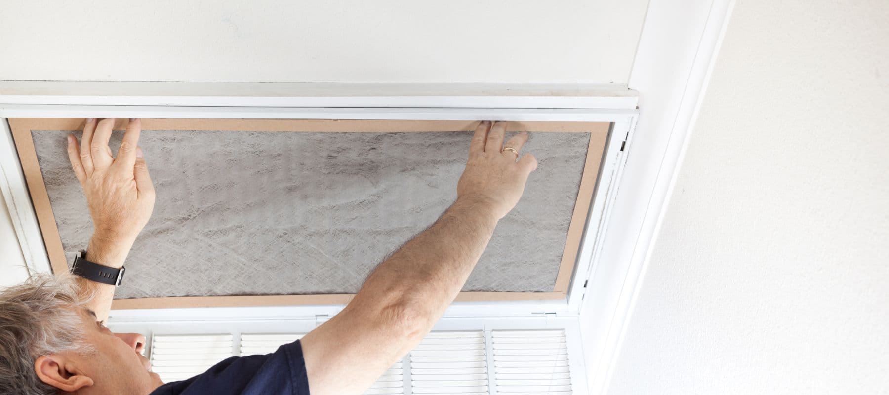 hvac technician reaching up to replace extremely dirty and full air filter