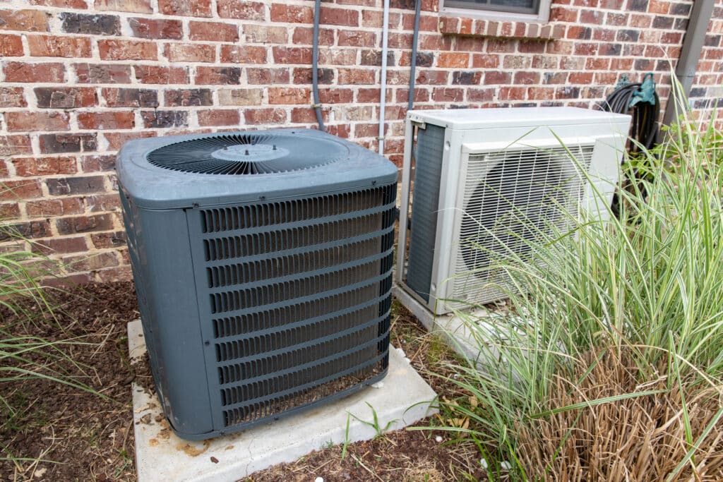 HVAC Air Conditioner Compressor and a Mini-split system together next to each other, next to a brick home