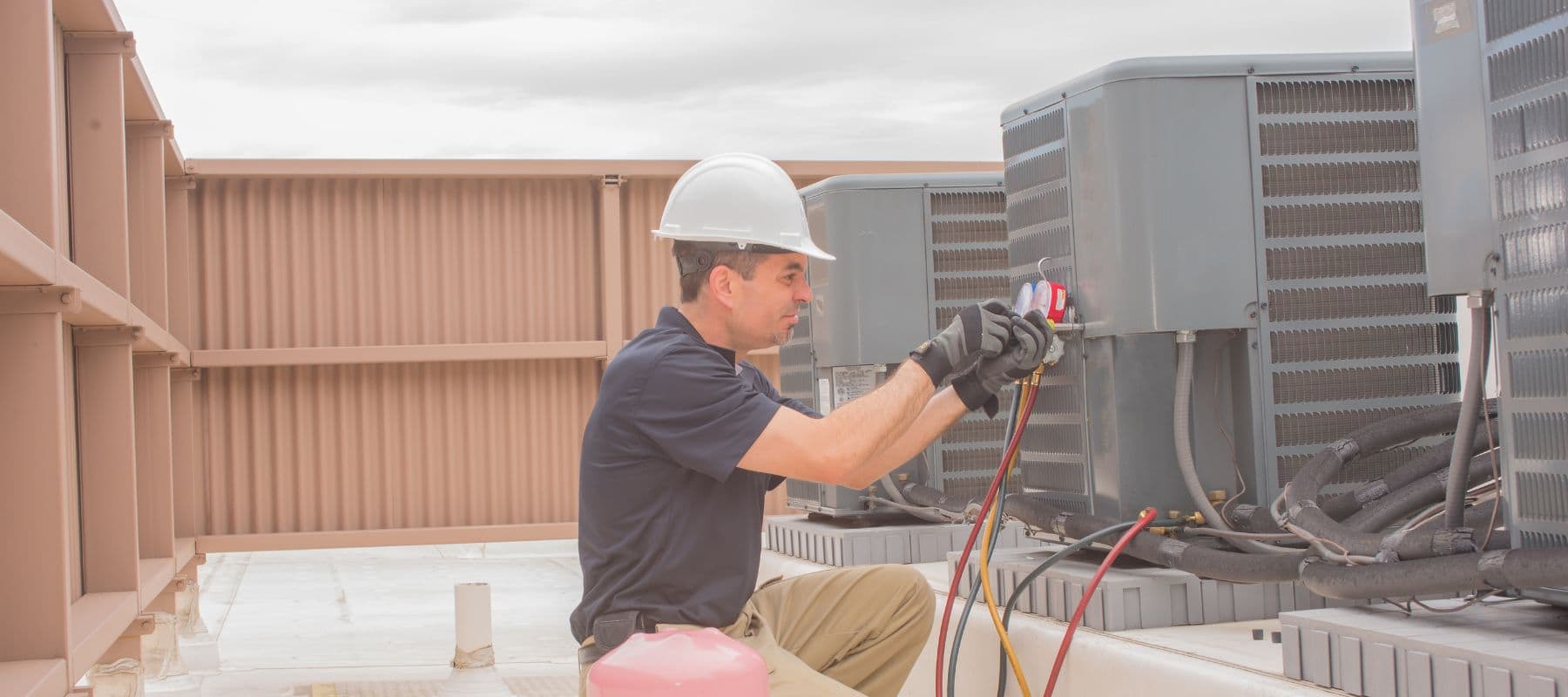 hvac technician wearing a hard hat and gloves while performing repairs on outdoor hvac units that are positioned on the top of a commercial building