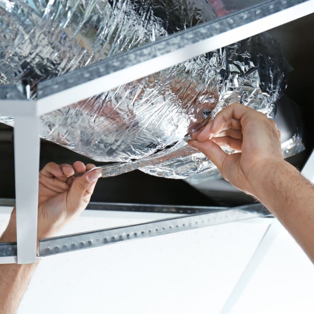 hands reaching up adding silver tape to air duct