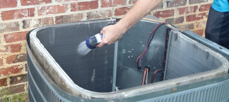 man spraying down the inside of an ac condenser unit installed outside a red brick home