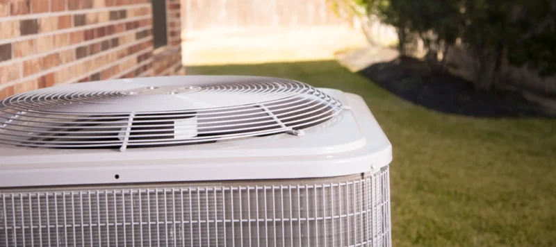 Close-up view of an outdoor central air conditioning unit next to a brick house, set in a neatly maintained backyard
