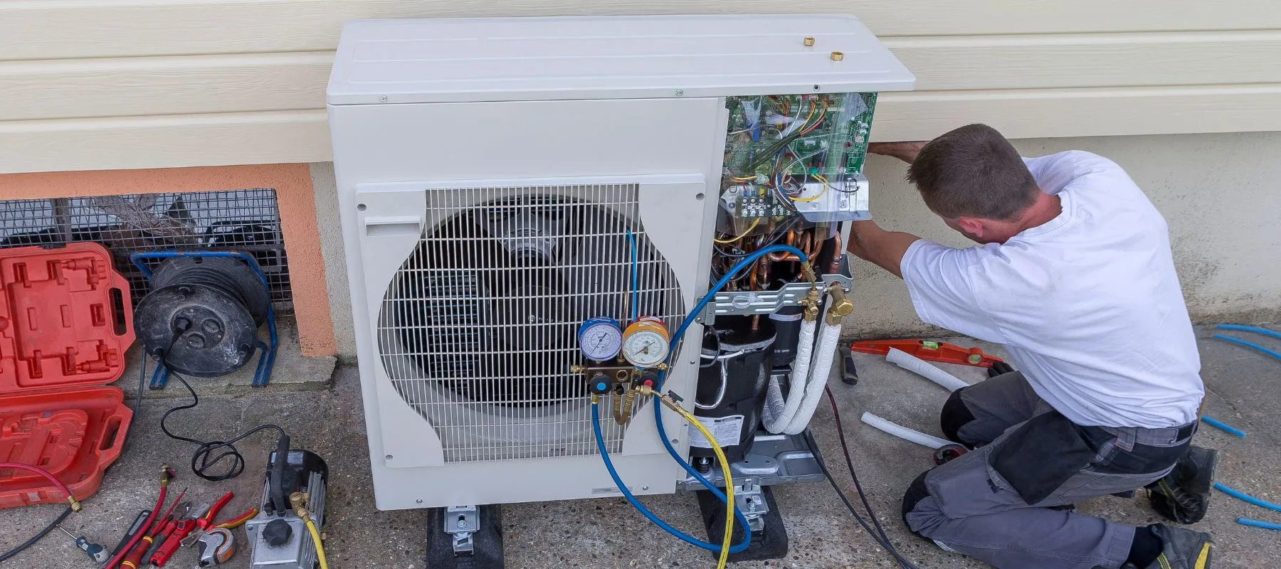 HVAC technician servicing a heat pump unit outside a home with tools nearby
